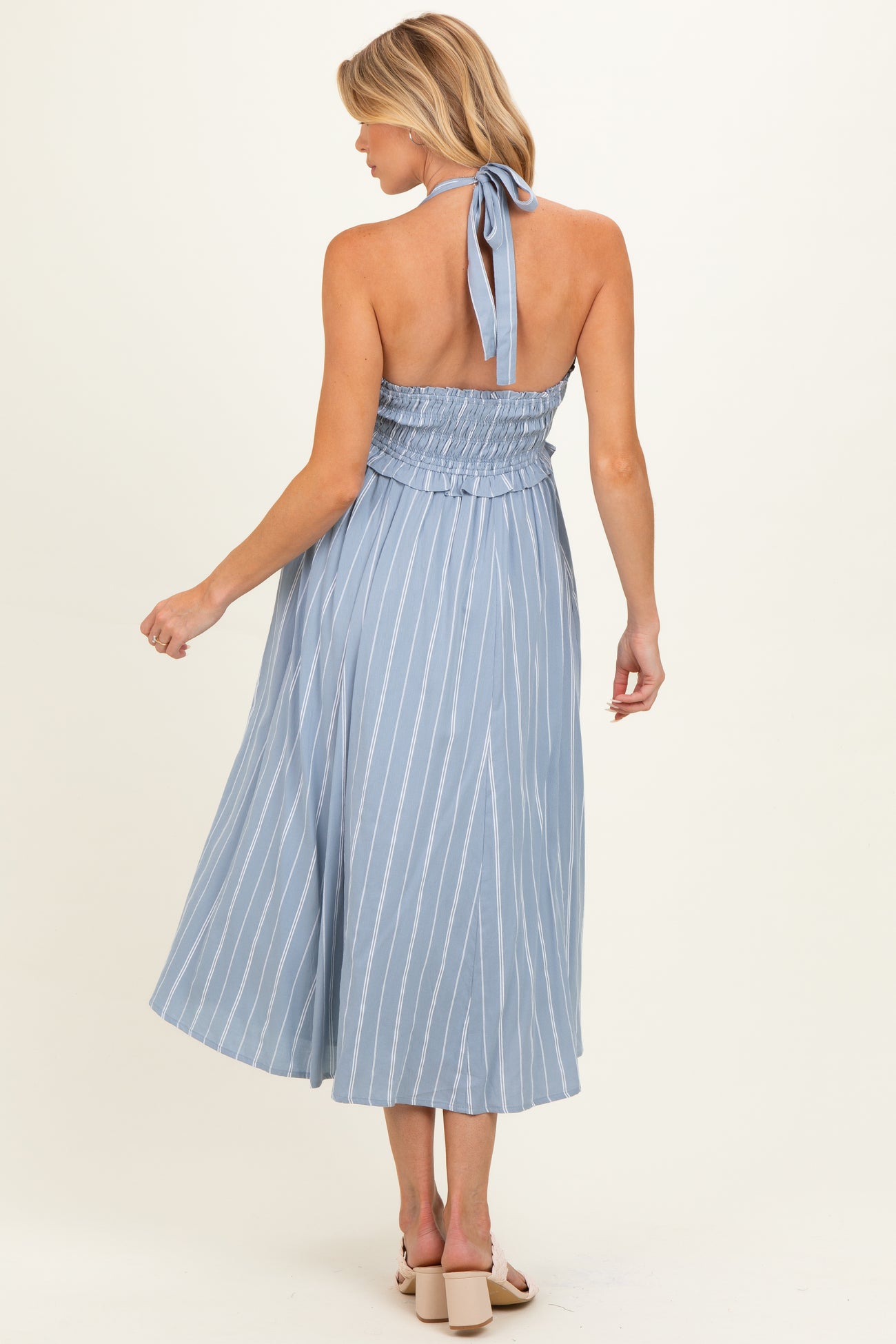 woman wearing a light blue maternity dress with white stripes and a halter neckline, showing her back