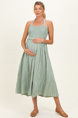 woman wearing a green striped maternity dress with smocked bodice and holding her baby bump