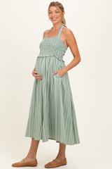 woman wearing a light green striped maternity dress with smocked bodice and pockets, holding her baby bump