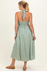 woman wearing a sleeveless green striped maternity dress with a smocked bodice and halter neck tie, shown from the back