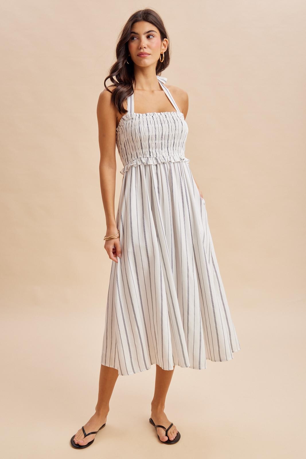 woman wearing a white striped midi dress with a smocked bodice and adjustable halter neck straps