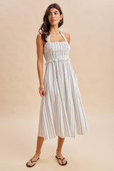 woman wearing a white striped midi dress with a smocked bodice and adjustable halter neck straps