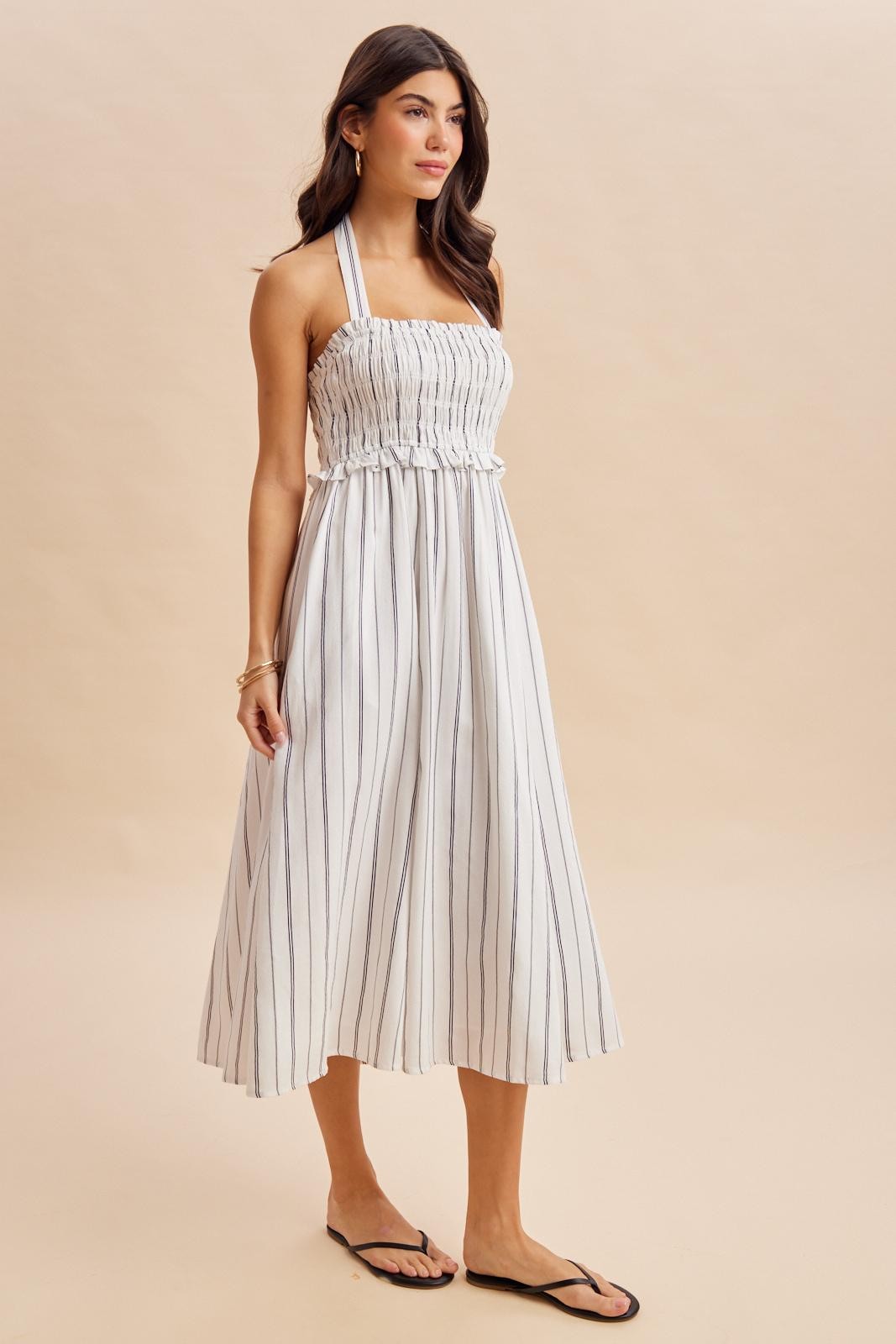 woman wearing a striped halter neck midi dress with a smocked bodice and loose-fitting skirt