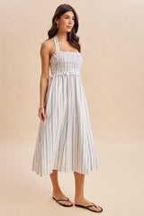 woman wearing a striped halter neck midi dress with a smocked bodice and loose-fitting skirt