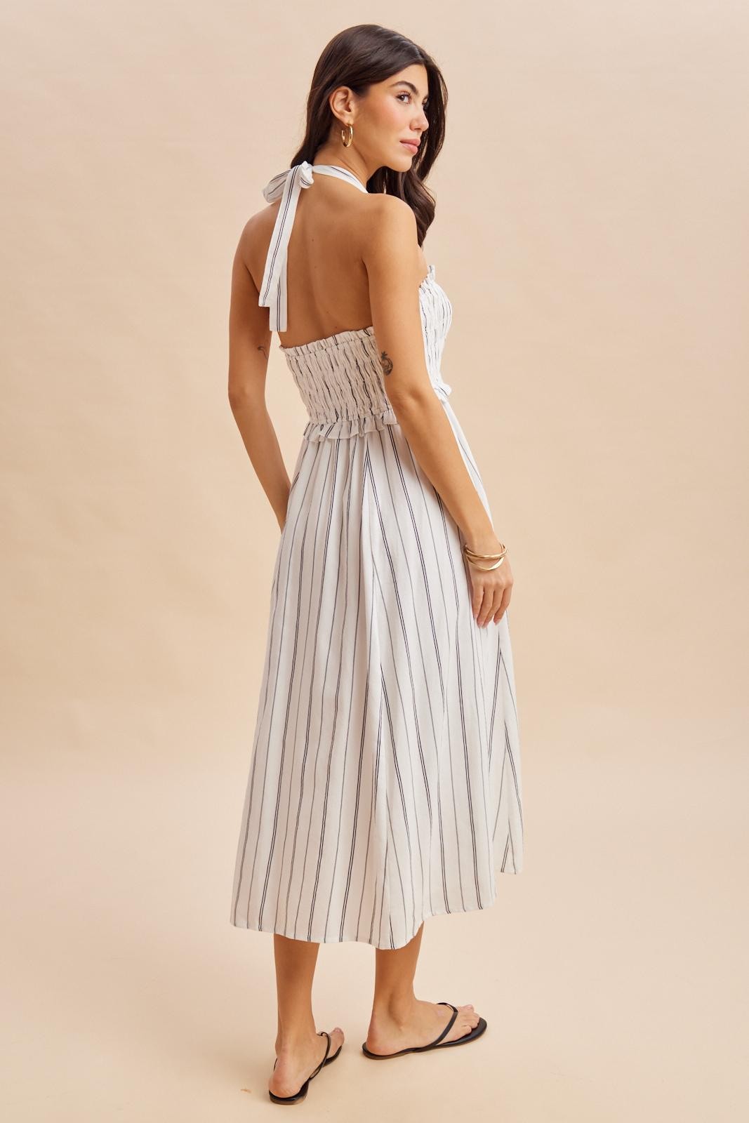 woman wearing a white and navy striped midi dress with a smocked bodice and tie straps, viewed from the back