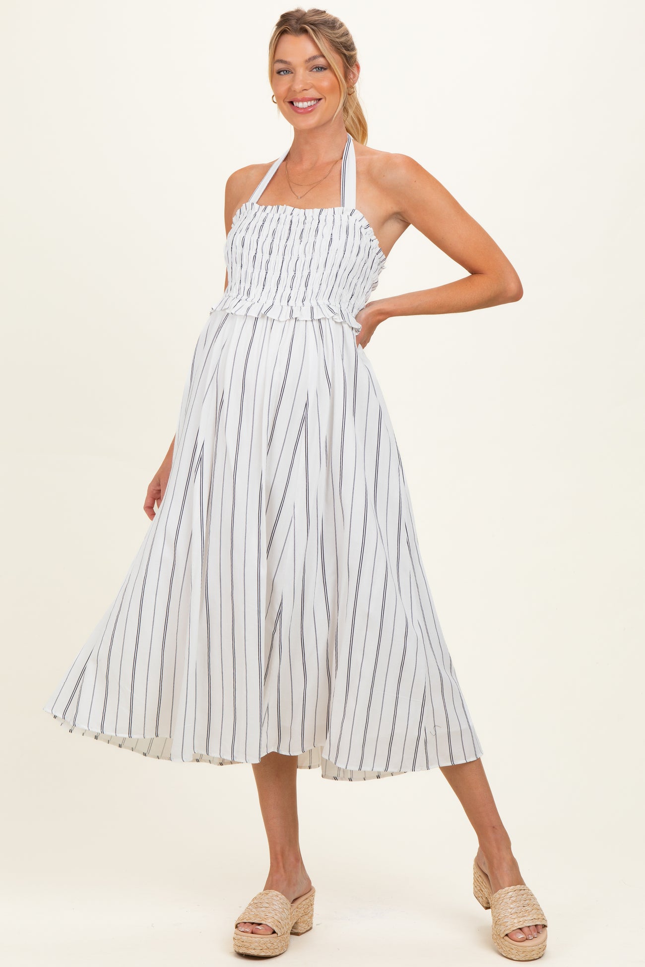 woman wearing a white and navy striped maternity dress with a smocked bodice and a flowing skirt, smiling and posing