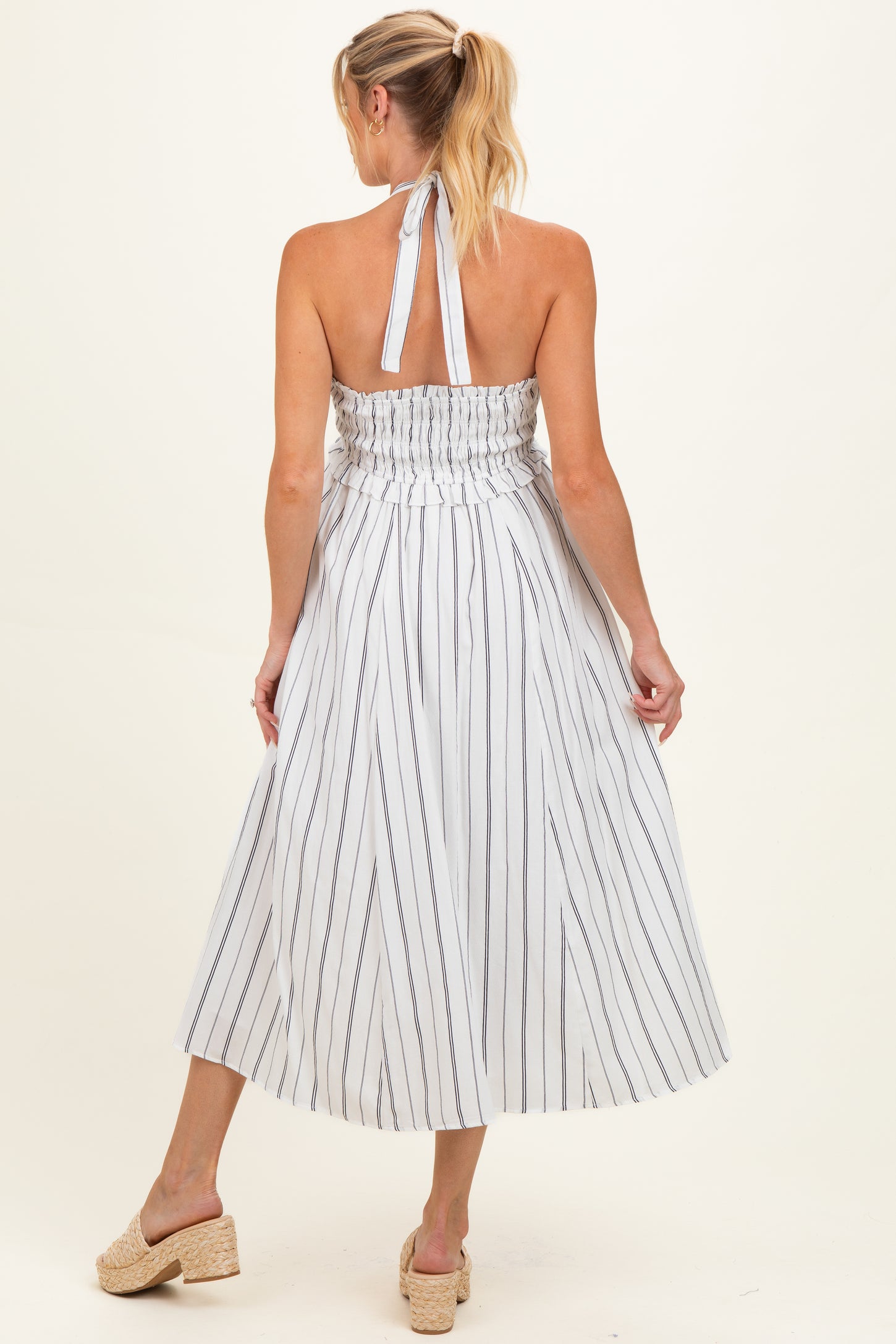 woman wearing a striped halter neck maternity dress with a smocked back and flowing midi skirt