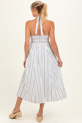 woman wearing a striped halter neck maternity dress with a smocked back and flowing midi skirt