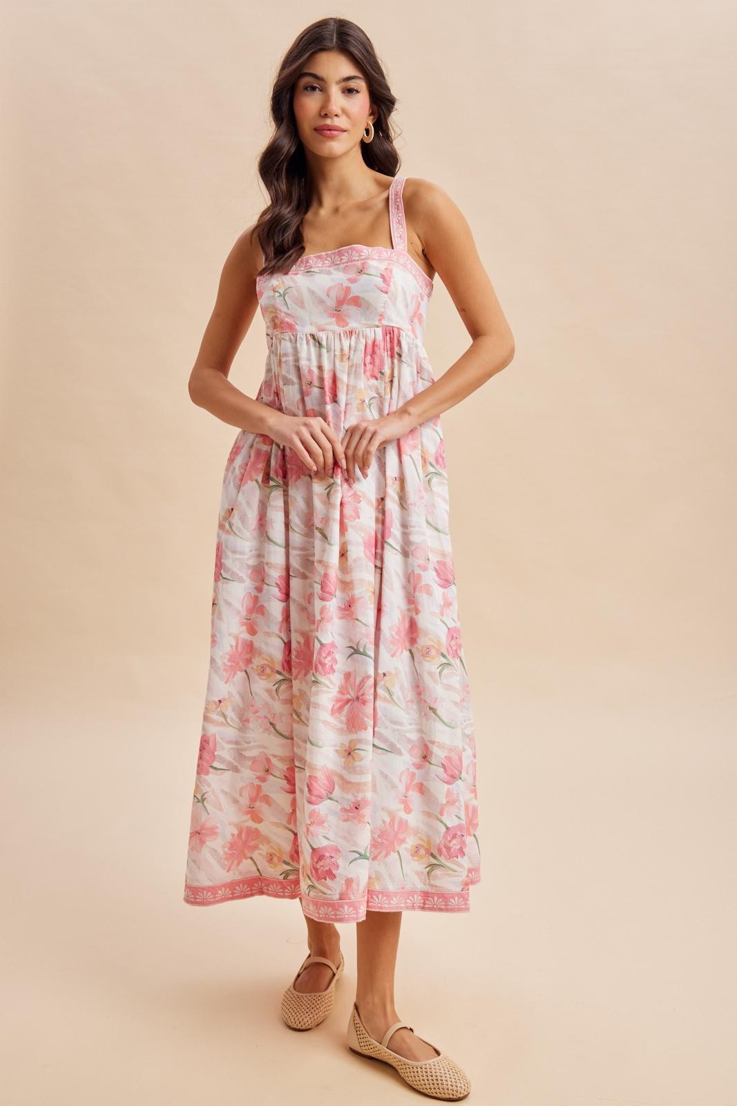 woman wearing a floral maxi dress with pink and white patterns and adjustable straps, standing with hands at her waist