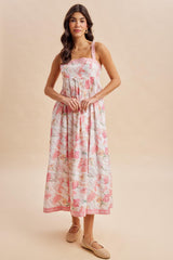 woman wearing a floral maxi dress with pink and white patterns and adjustable straps, standing with hands at her waist