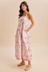 woman wearing a floral midi dress with pink and white hues and pockets, styled with woven flats