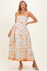 woman wearing a floral maternity maxi dress in orange and yellow with spaghetti straps and a flowing silhouette