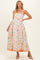 woman wearing a floral maternity maxi dress in orange and yellow with spaghetti straps and a flowing silhouette