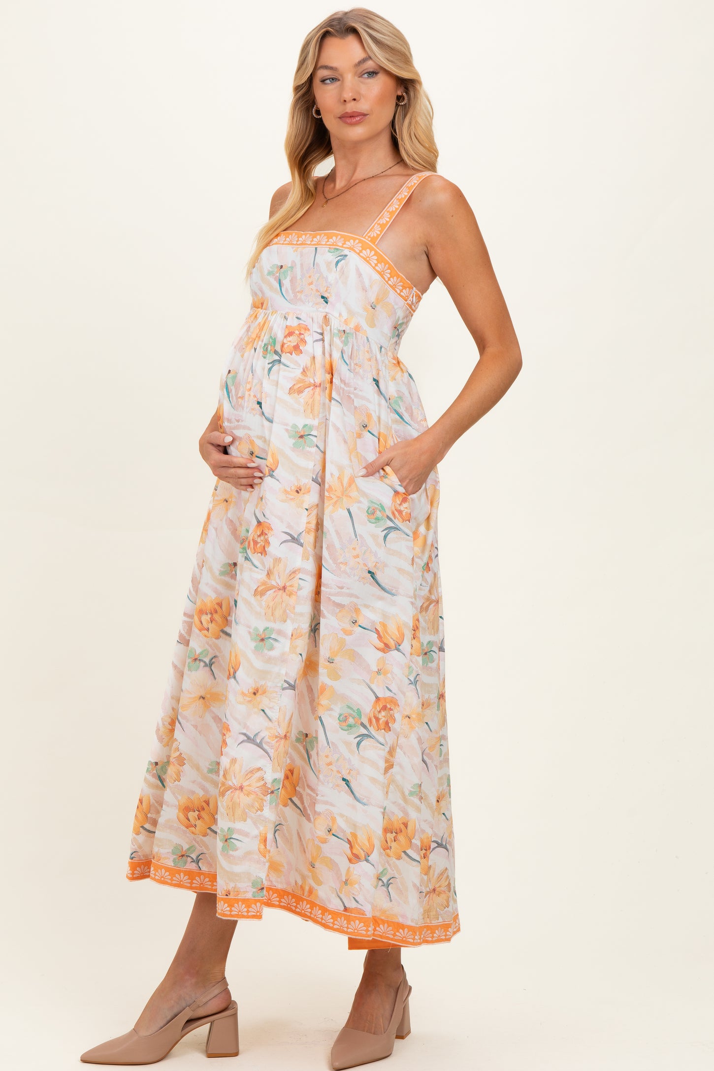 woman wearing a floral maternity maxi dress with adjustable straps and pockets, showcasing her baby bump