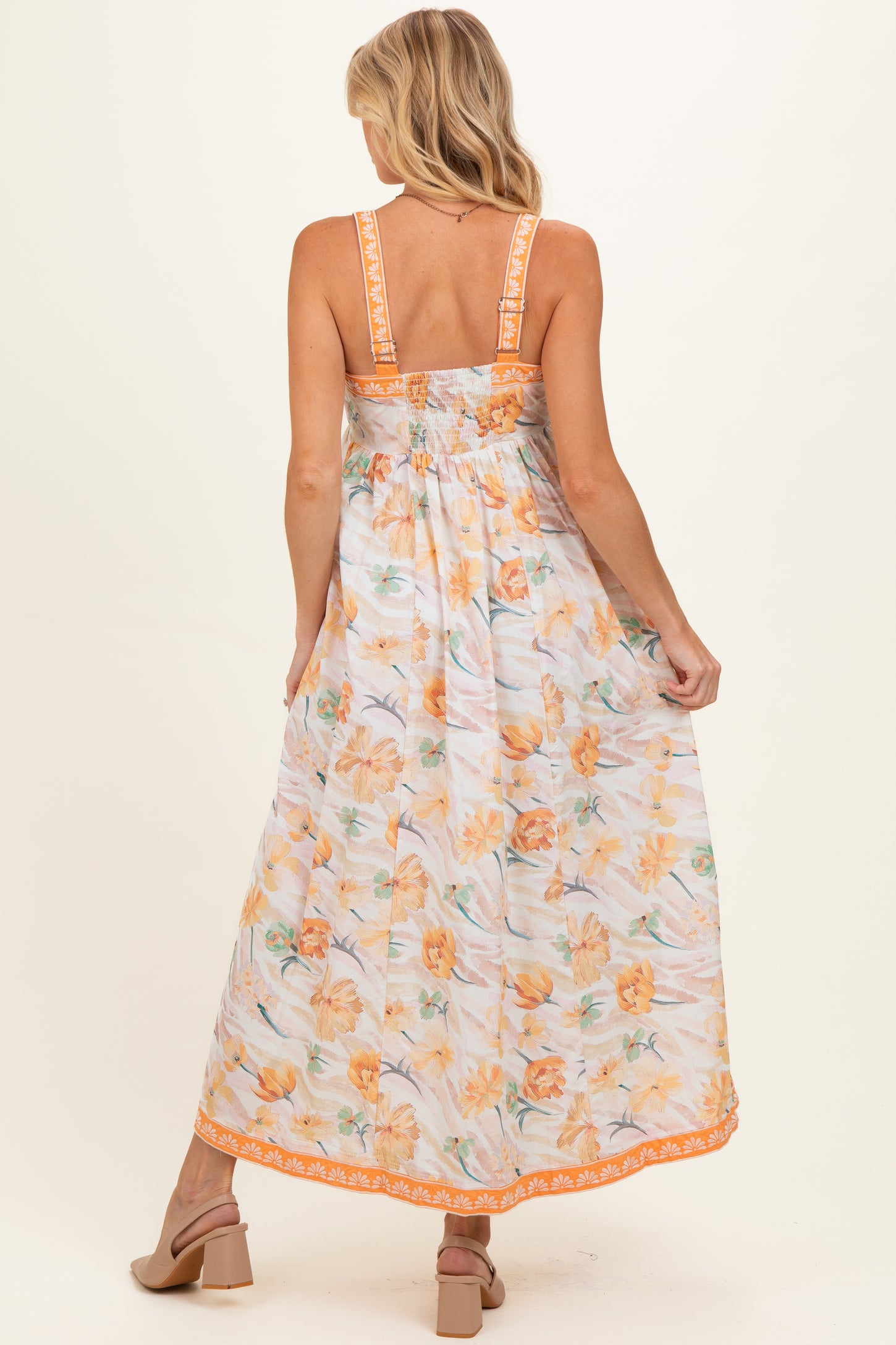 woman wearing a floral maternity maxi dress with a smocked back and orange trim, showing a baby bump