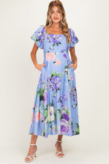 woman wearing a light blue floral maternity dress with short puff sleeves and pockets, showcasing her baby bump
