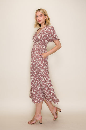 woman wearing a mauve floral midi dress with short puff sleeves and pockets, standing in profile against a neutral background