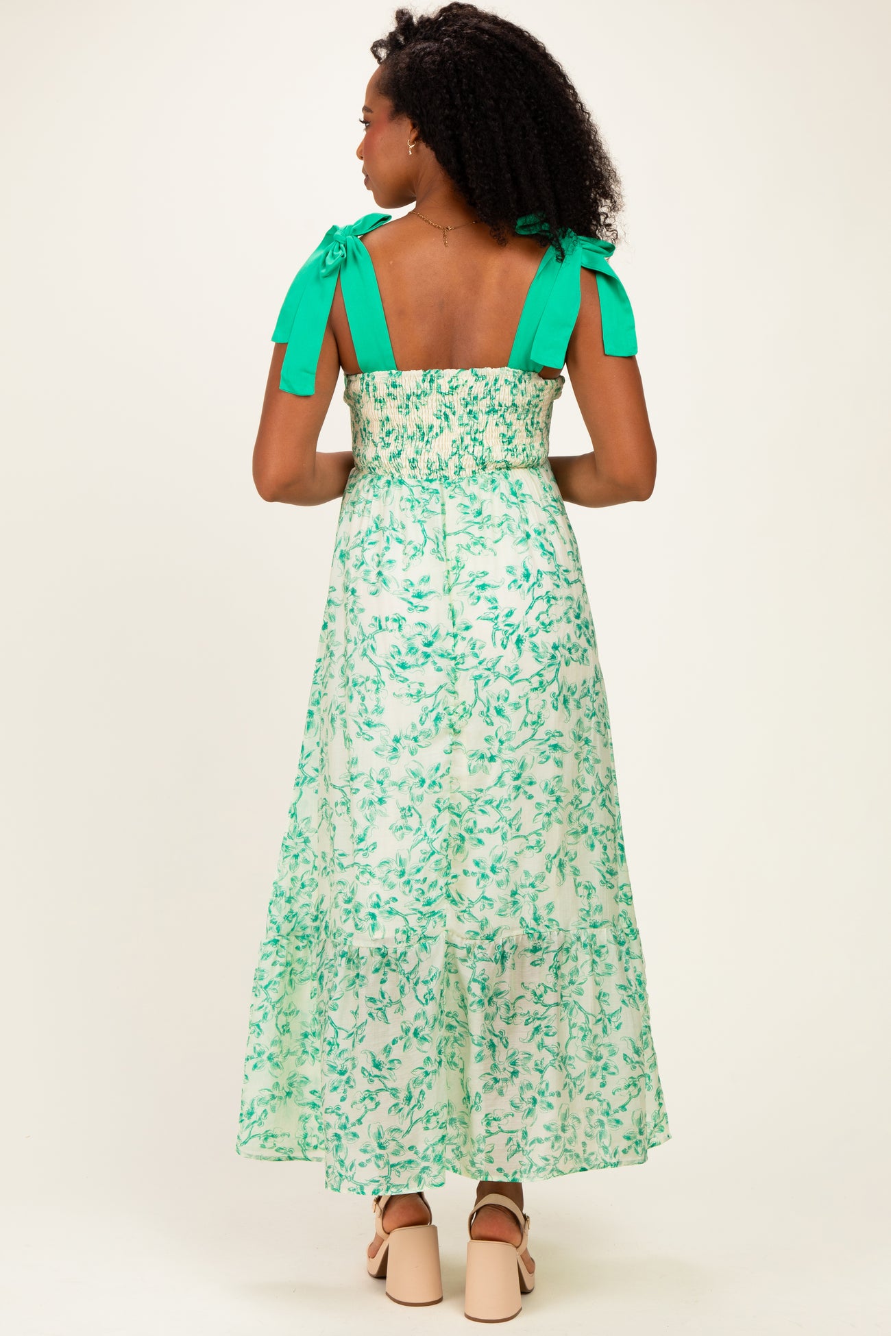 woman wearing a green floral maxi dress with smocked back and bow shoulder straps, shown from the back