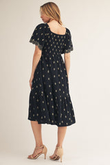woman wearing a black midi dress with a tiered skirt and embroidered short sleeves, view from the back