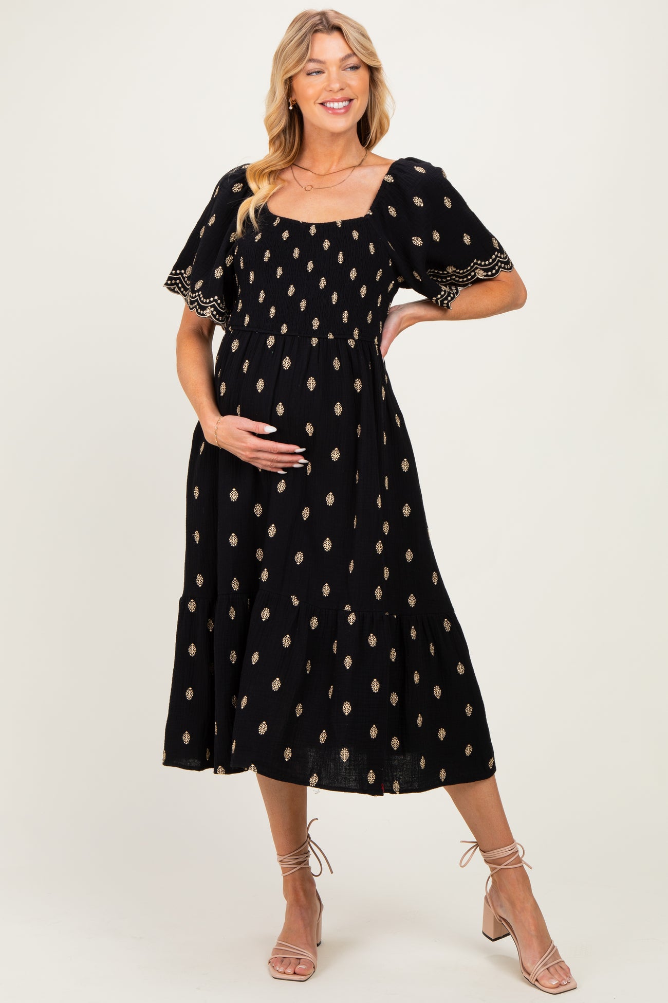 woman wearing a black maternity dress with gold patterns and short sleeves, gently cradling her baby bump