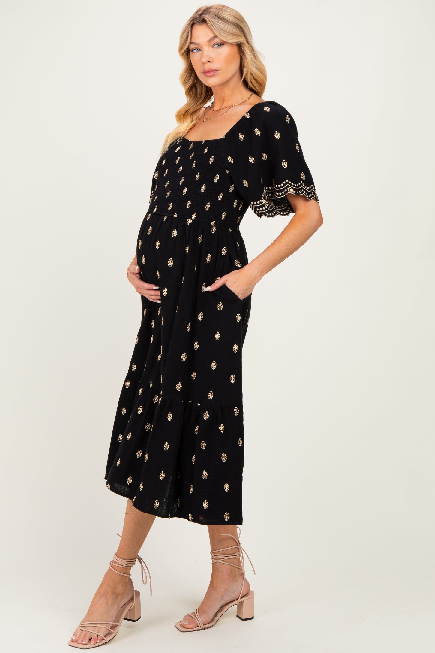 woman wearing a black maternity maxi dress with gold print, short sleeves, and pockets, showing her baby bump