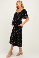 woman wearing a black maternity maxi dress with gold print, short sleeves, and pockets, showing her baby bump