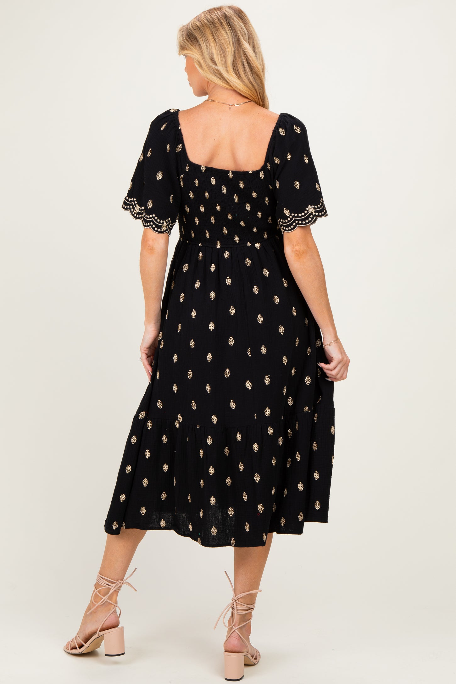 woman wearing a black maternity dress with gold floral patterns and short puff sleeves, shown from the back