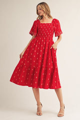woman wearing a red midi dress with short puff sleeves, square neckline, and decorative patterns, standing in a slight pose