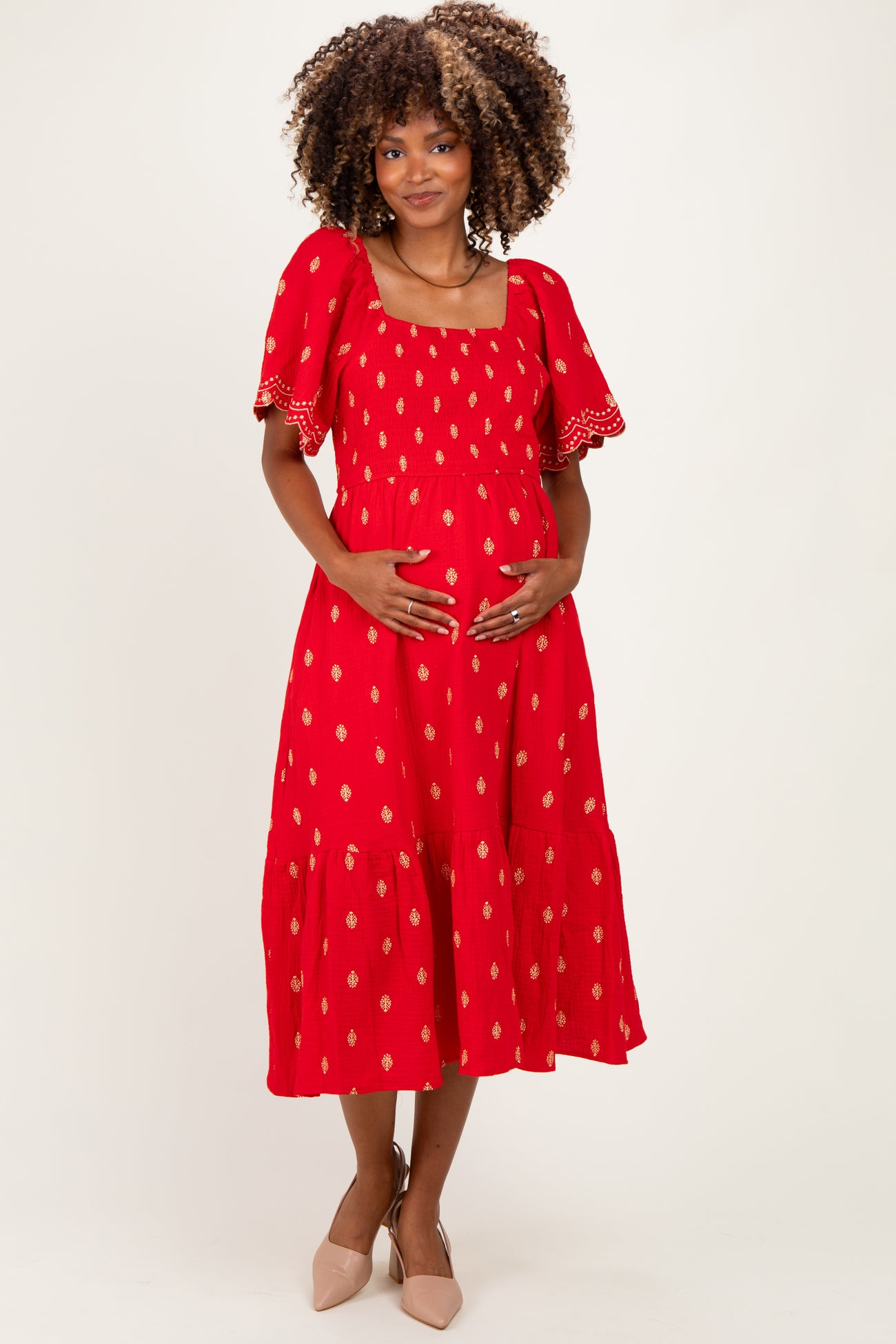 woman wearing a red patterned maternity dress with puff sleeves and holding her baby bump
