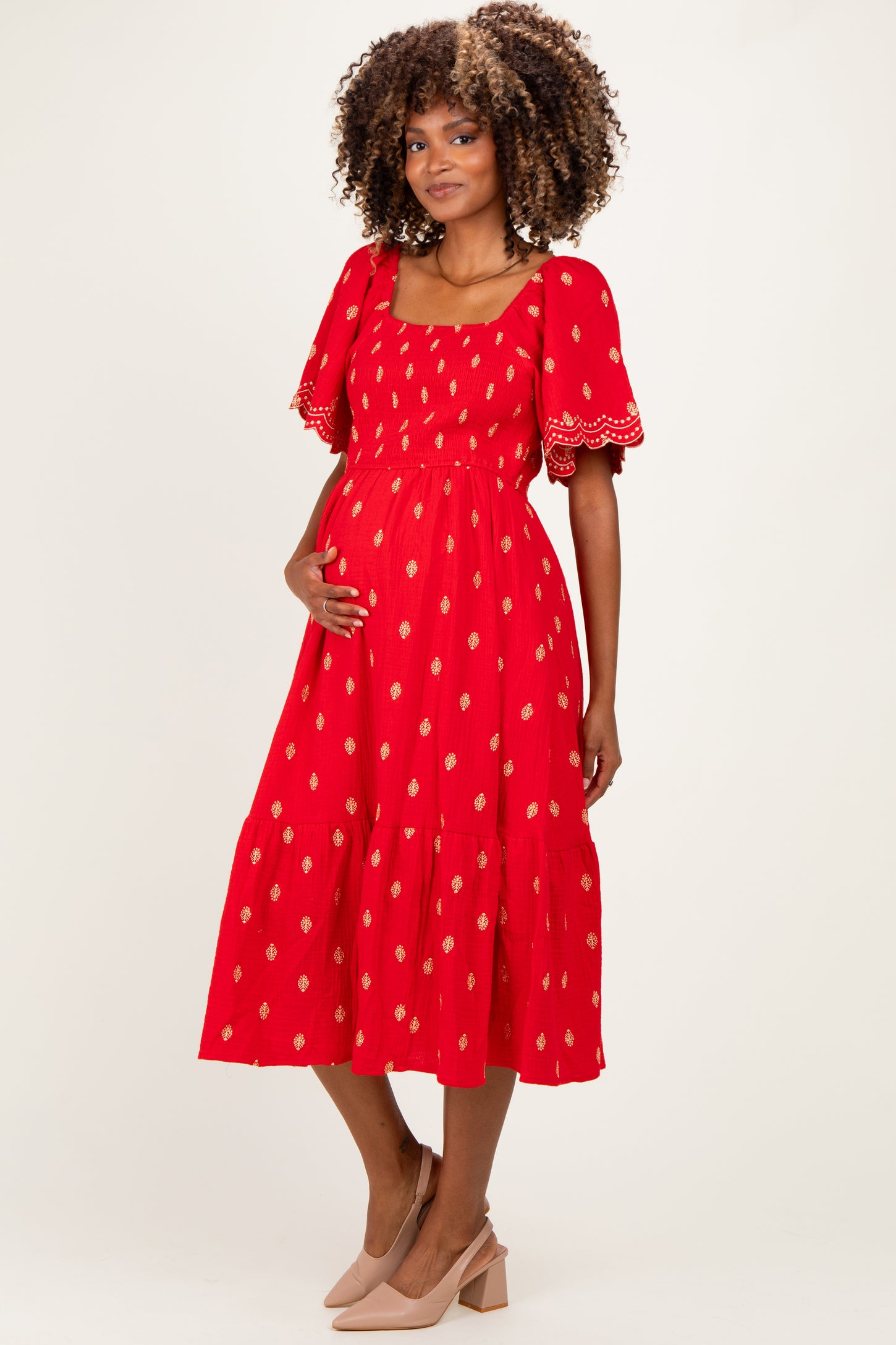 woman wearing a red printed maternity dress with short puff sleeves and a fitted bodice, showing off her baby bump