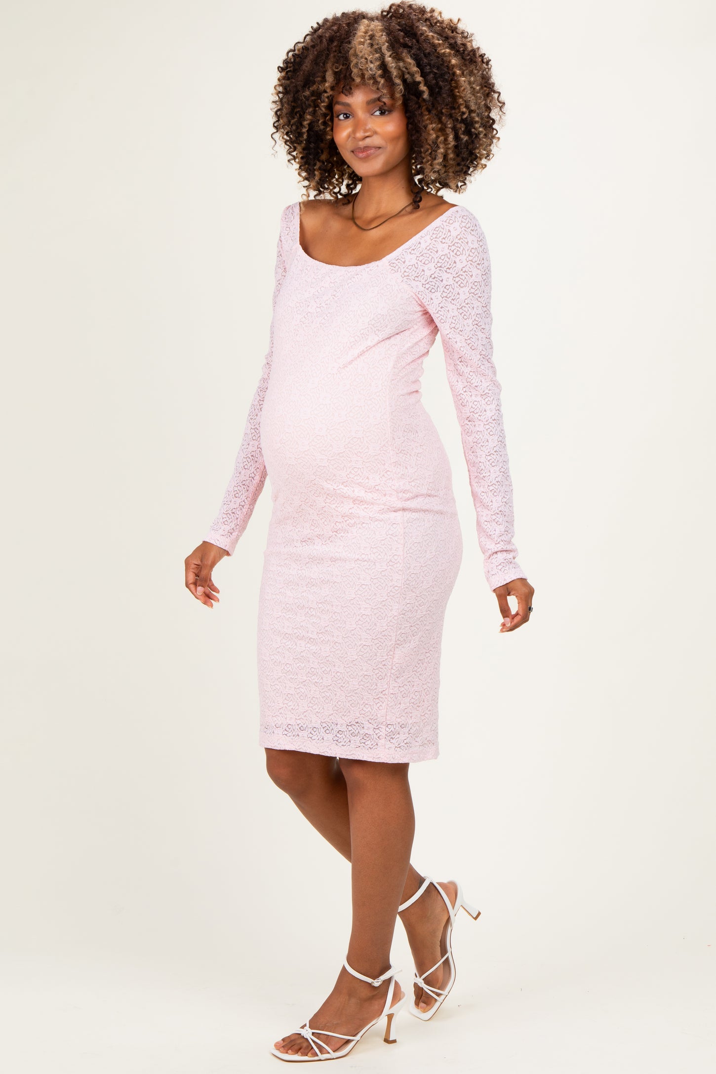 woman wearing a light pink long sleeve lace maternity dress, showing a visible baby bump and standing confidently