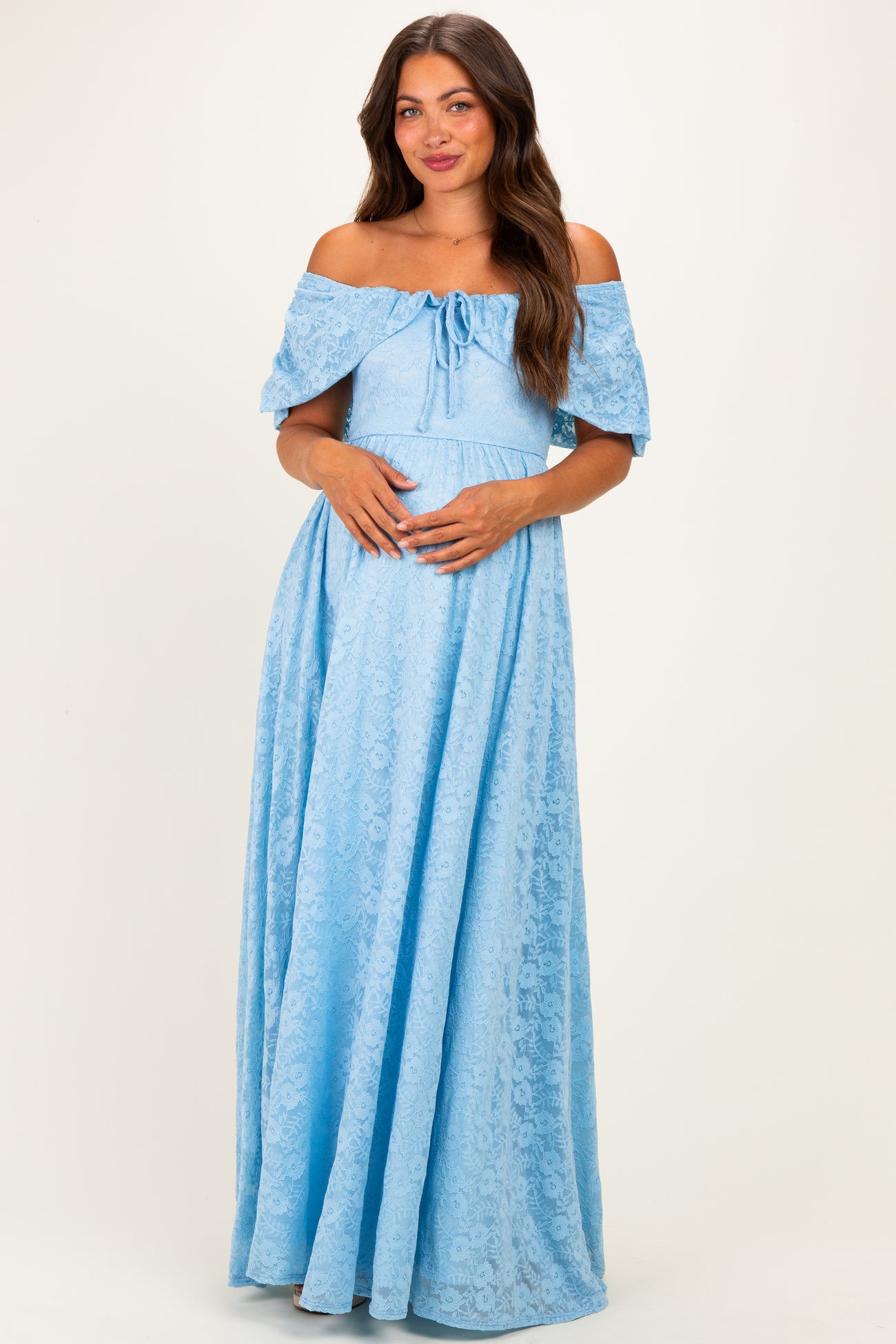 woman wearing a light blue off-the-shoulder lace maternity dress and holding her baby bump