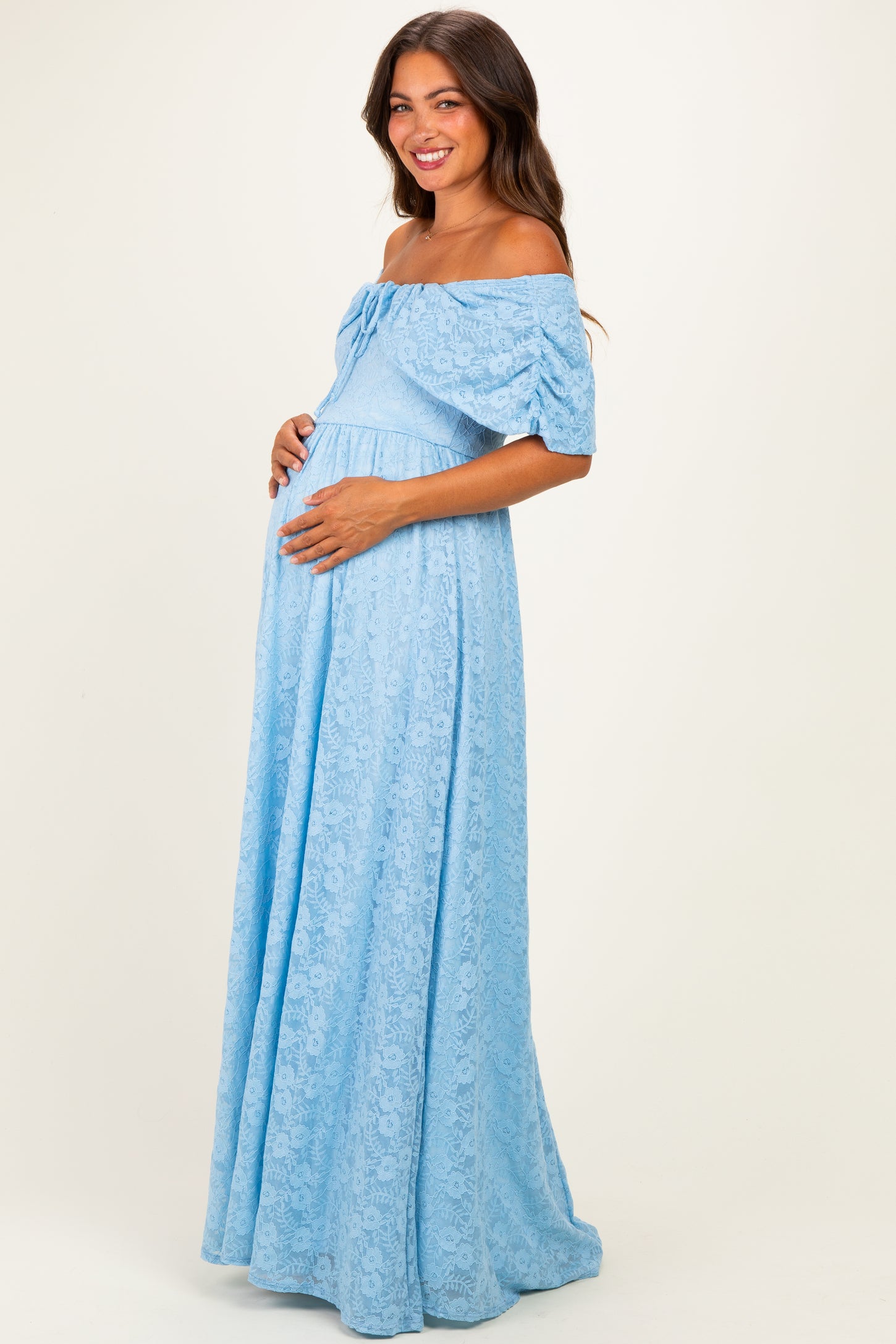 woman wearing a light blue off-the-shoulder lace maternity dress and holding her baby bump