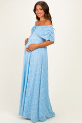woman wearing a light blue off-the-shoulder lace maternity dress and holding her baby bump