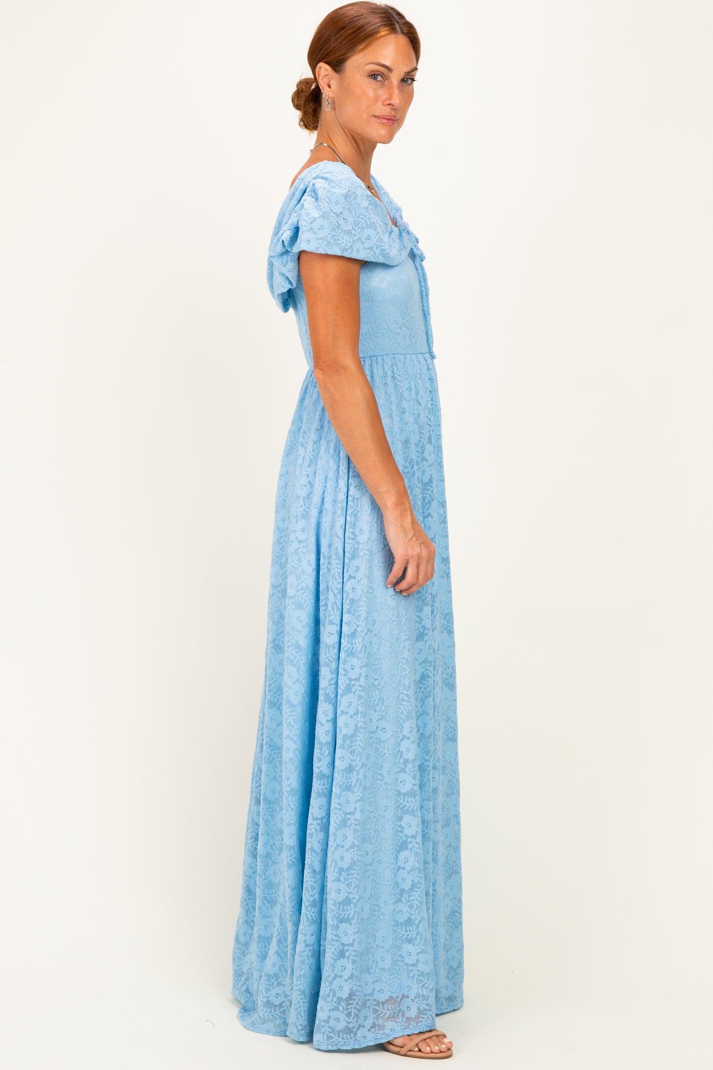 woman wearing a light blue lace maxi dress with short sleeves and a tied bow detail on the back