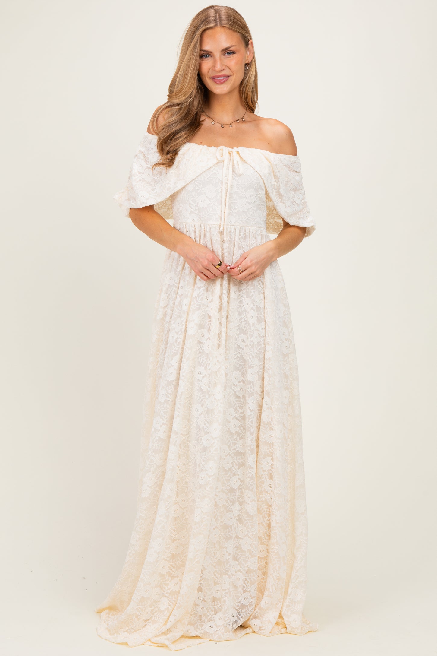 woman wearing a cream off-the-shoulder lace maxi dress with a tie detail at the bust
