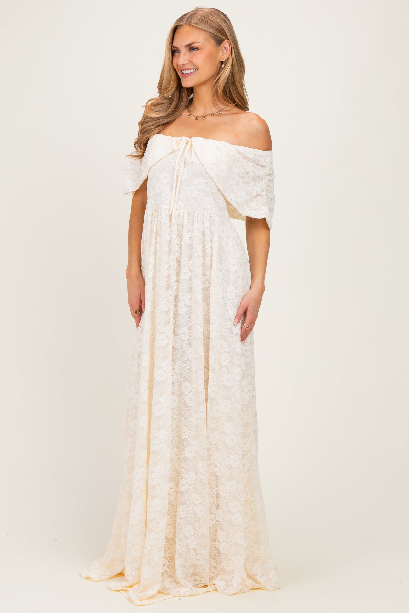 woman wearing a cream off-the-shoulder lace maxi dress with a drawstring waist and flowing skirt