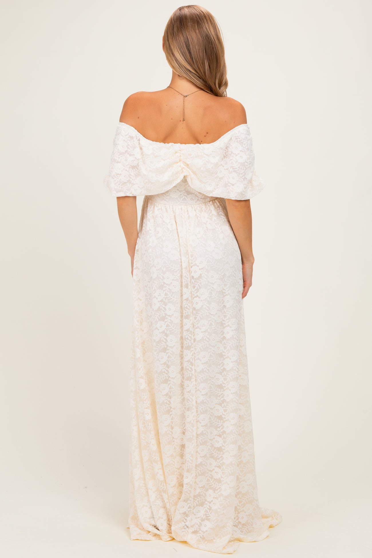 woman wearing a white off-the-shoulder maxi dress with lace detailing, shown from the back