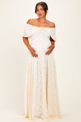 woman wearing a cream off-the-shoulder lace maternity maxi dress and cradling her baby bump
