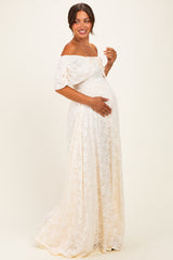 woman wearing an off-the-shoulder cream lace maternity dress and gently cradling her baby bump
