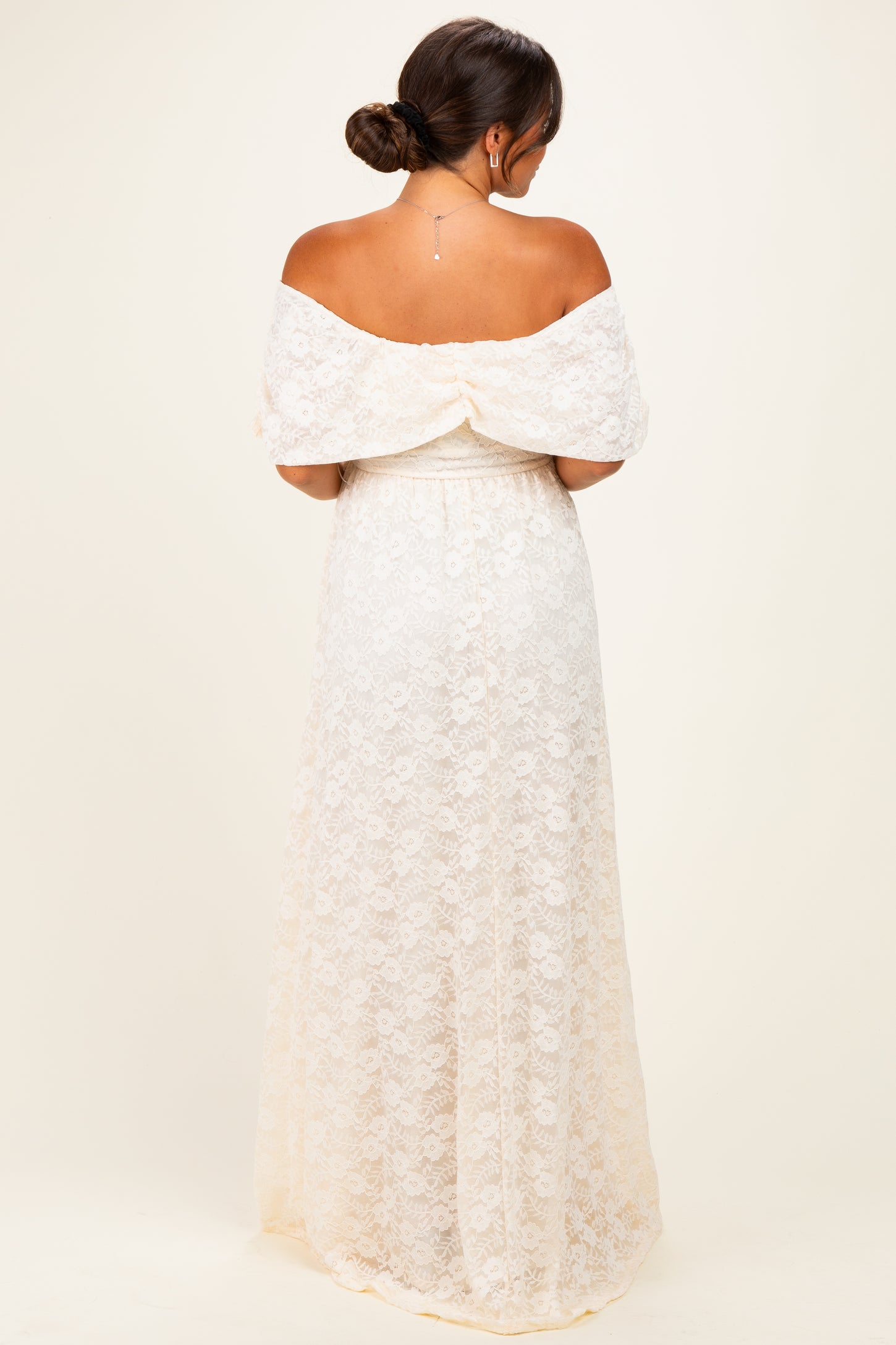 woman wearing a cream off-the-shoulder lace maternity gown with a flowing skirt and gathered bodice