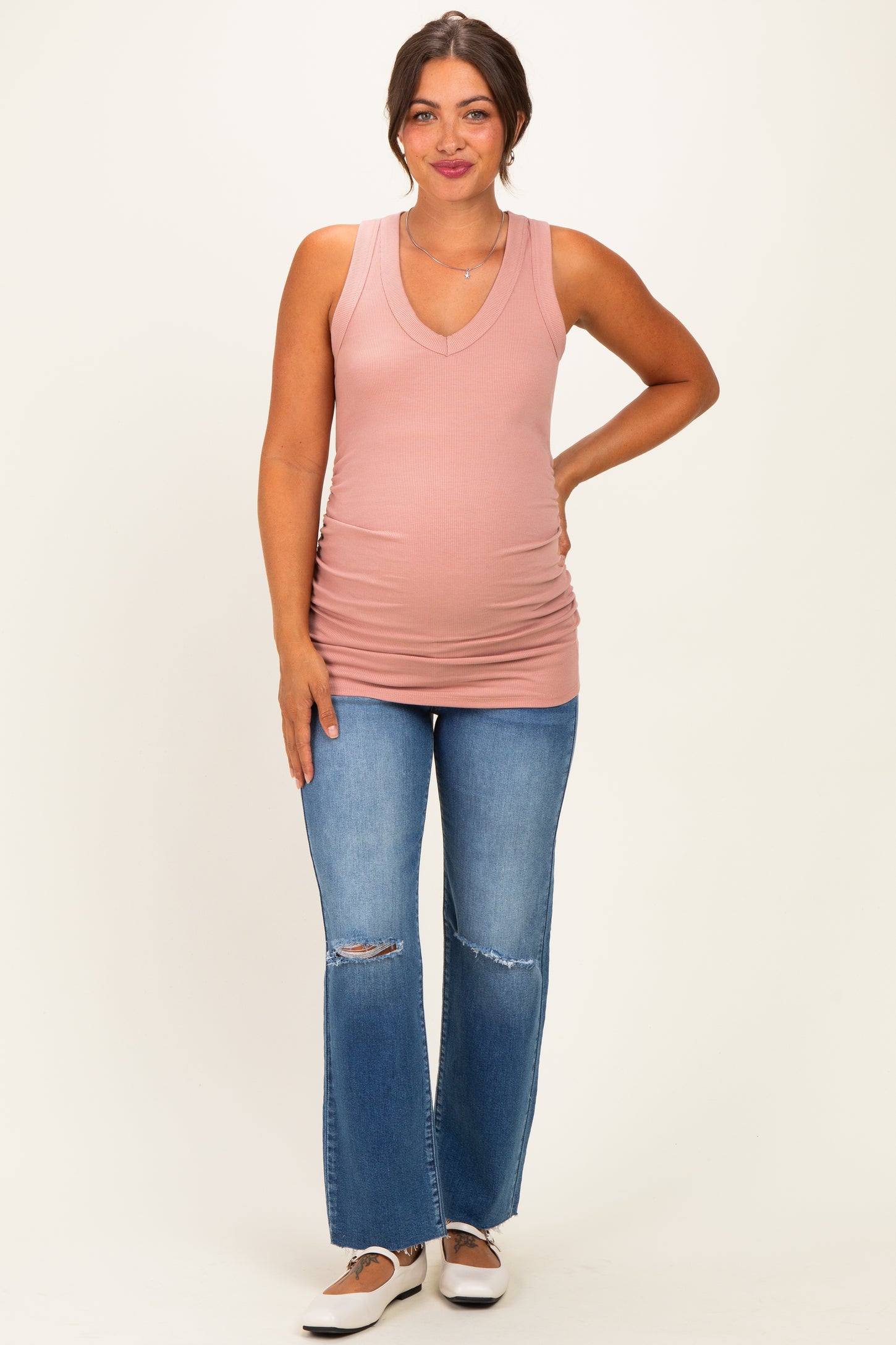woman wearing a pink ribbed tank top with a v-neck and revealing a baby bump, paired with distressed blue jeans