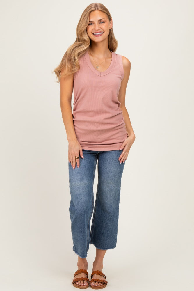 woman wearing a dusty rose sleeveless v-neck top and blue wide-leg jeans, smiling while posing on a light background
