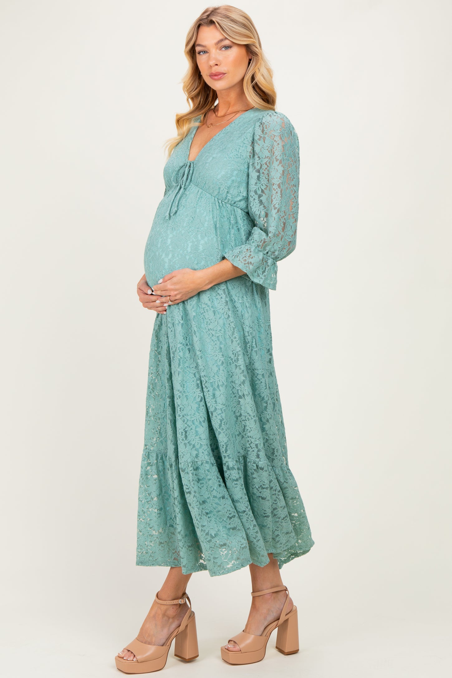 woman wearing a teal lace maternity dress with three-quarter sleeves and holding her baby bump