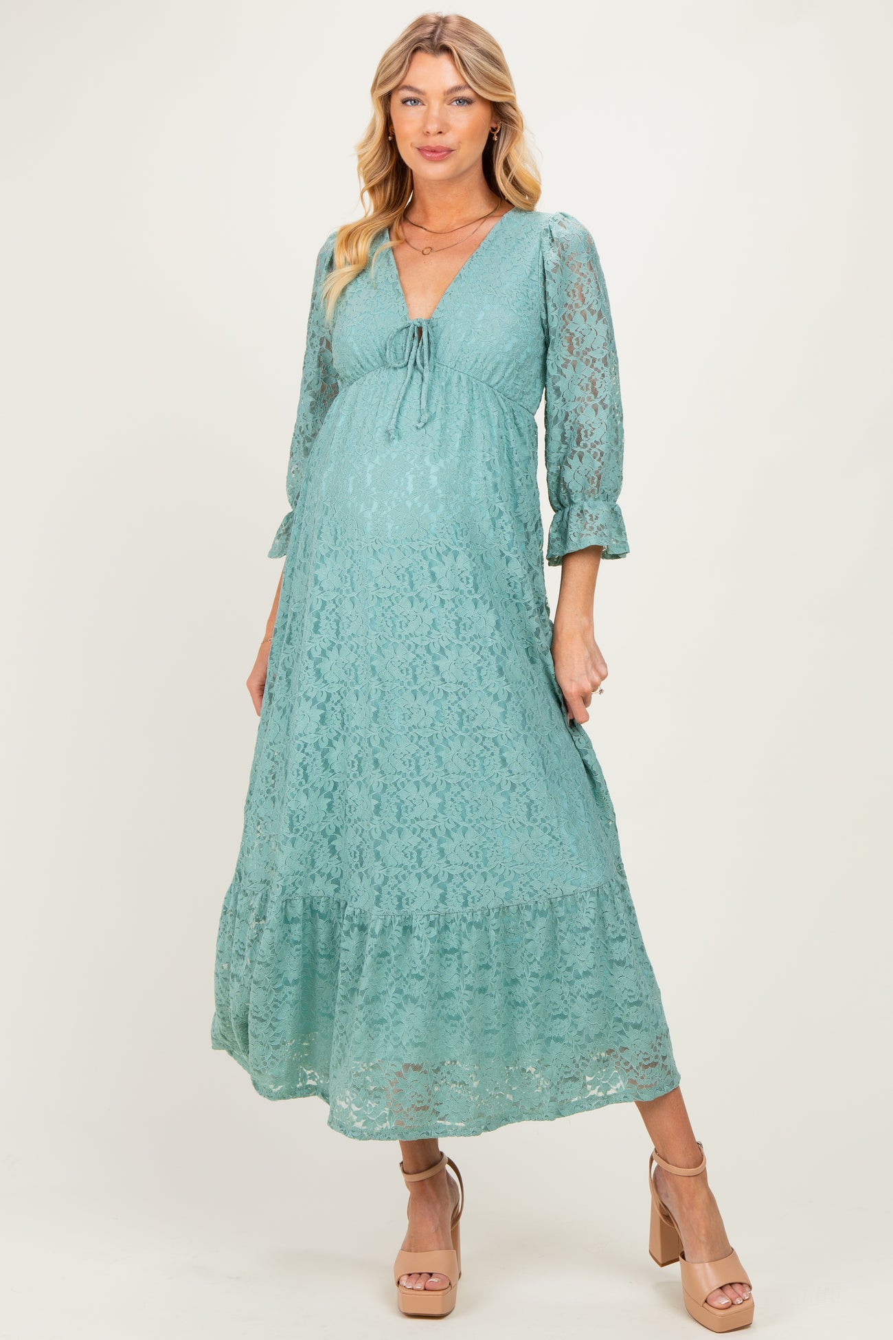 woman wearing a green lace maternity dress with 3/4 sleeves and a gathered waist, showing her baby bump
