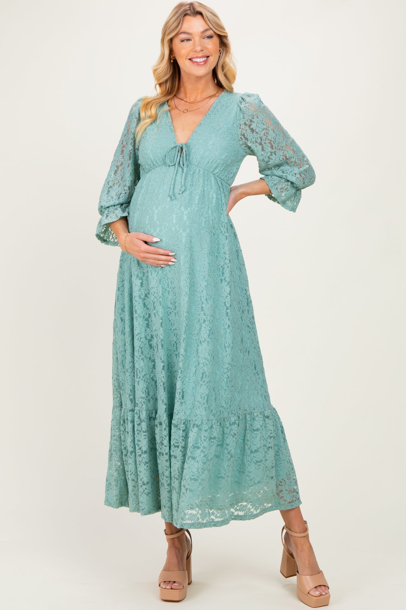 woman wearing a teal lace maternity dress with a plunging neckline and puff sleeves, holding her baby bump