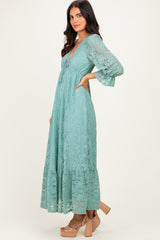 woman wearing a mint green lace maxi dress with long bell sleeves and a tiered hem, standing in profile