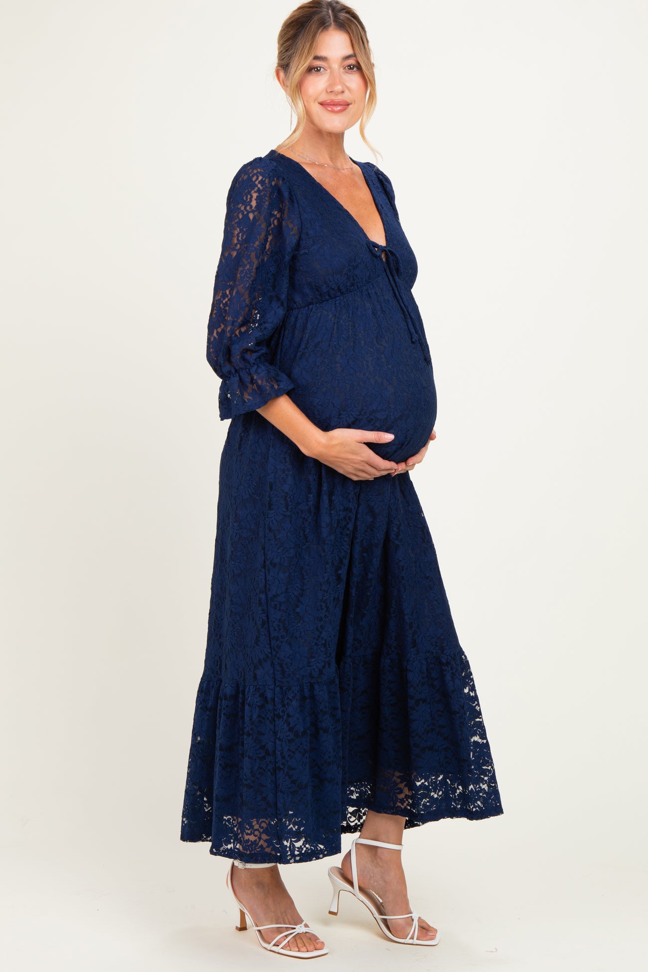 woman wearing a navy blue lace maternity dress with a tie detail and a visible baby bump