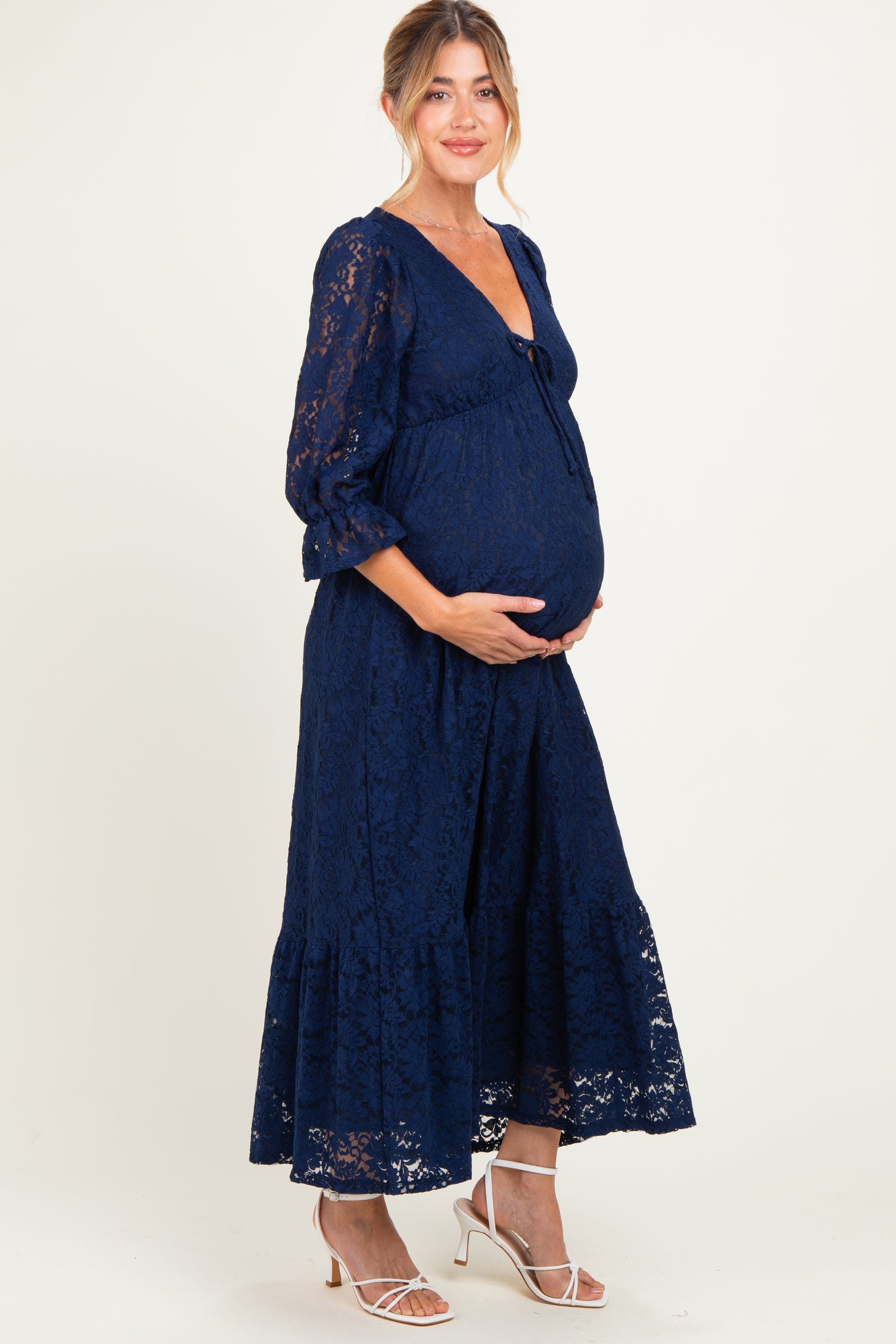 woman wearing a navy blue lace maternity dress with a tie detail and a visible baby bump