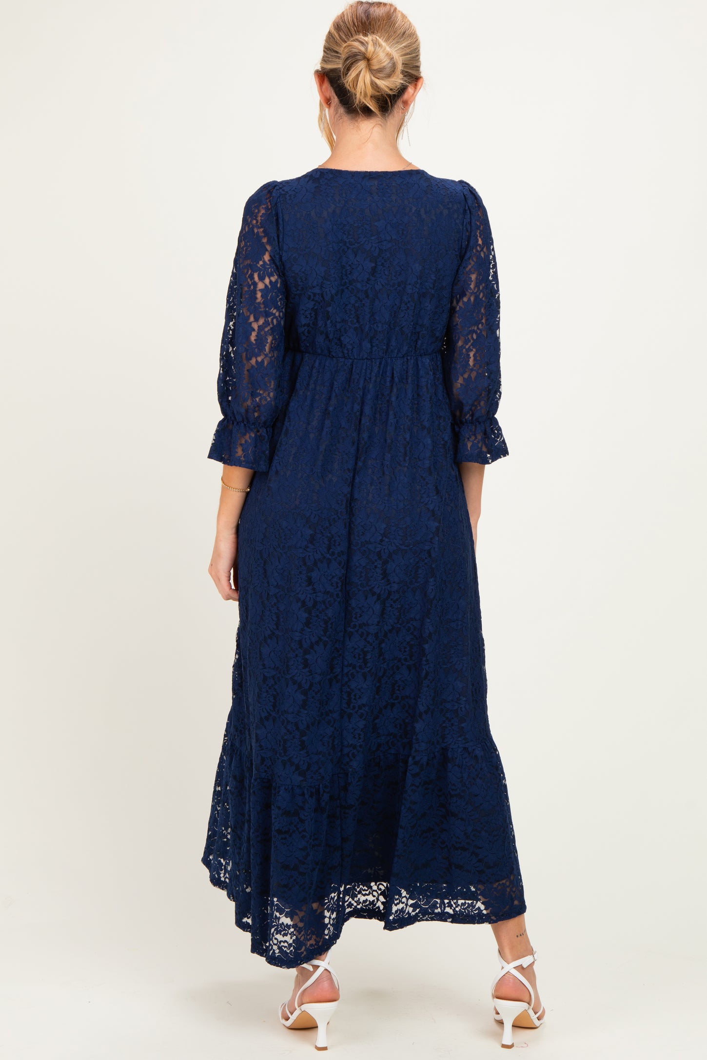 woman wearing a navy blue lace maternity dress with three-quarter sleeves and a flowy skirt, showing a baby bump